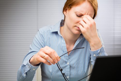 パソコンの前で眼鏡をはずし目に手をやる女性