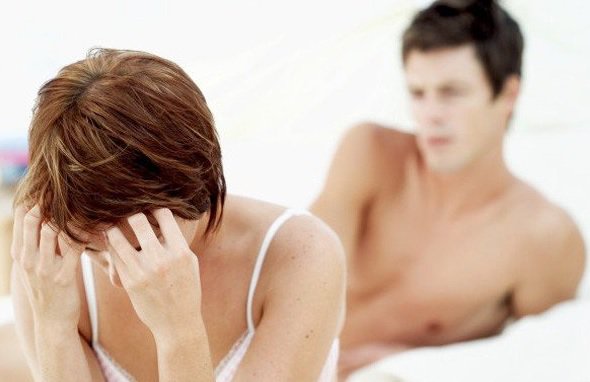 ベッドで頭を抱えてうつむく女性と背後に男性