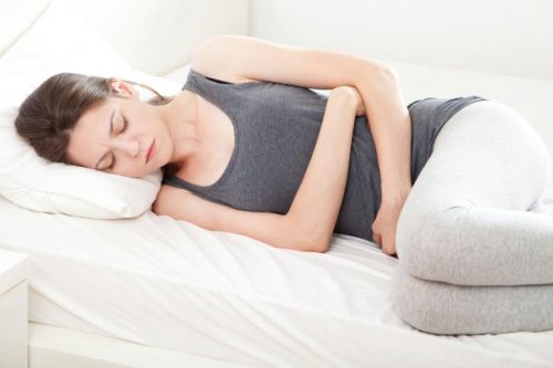 ベッドでお腹を抑える女性