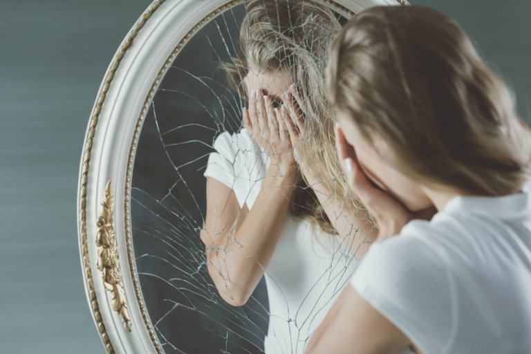 割れた鏡の前で顔を覆う女性