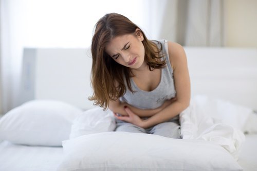 白いベッドの上で腹部の痛みに耐える女性