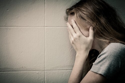 壁際で顔を覆う女性
