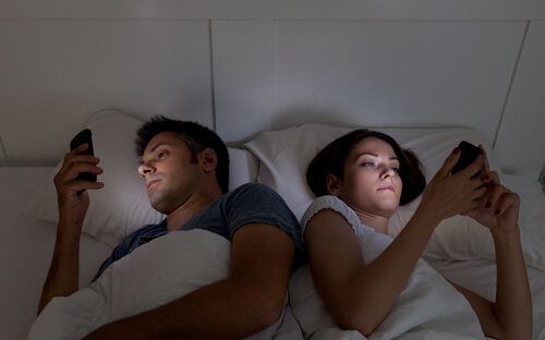 寝ながらスマートフォンをみるカップル スマートフォンの悪影響