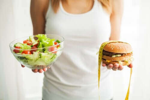 肥満の予防に役立つ食品のタイプとは？　サラダとハンバーガーを持つ女性
